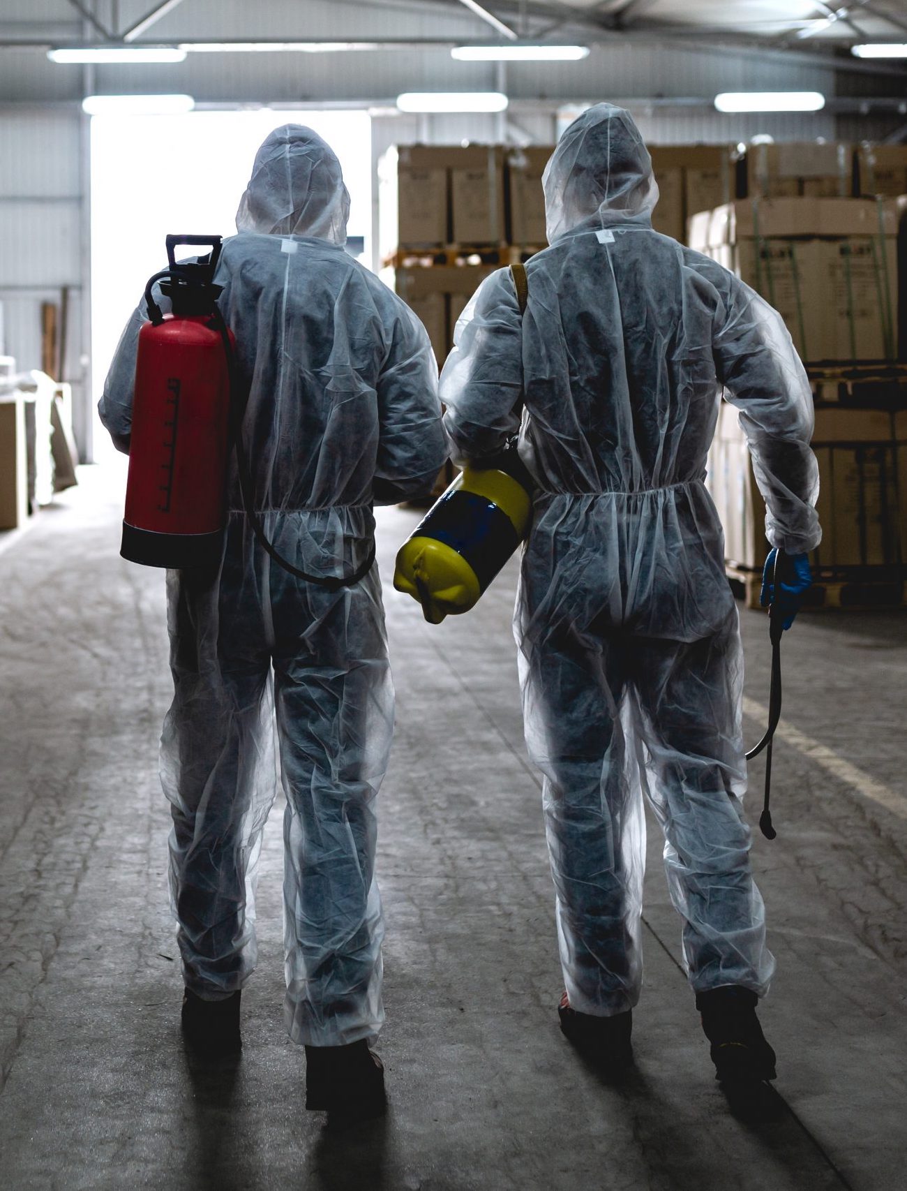 Two men in hazmat suits cleaning a warehouse